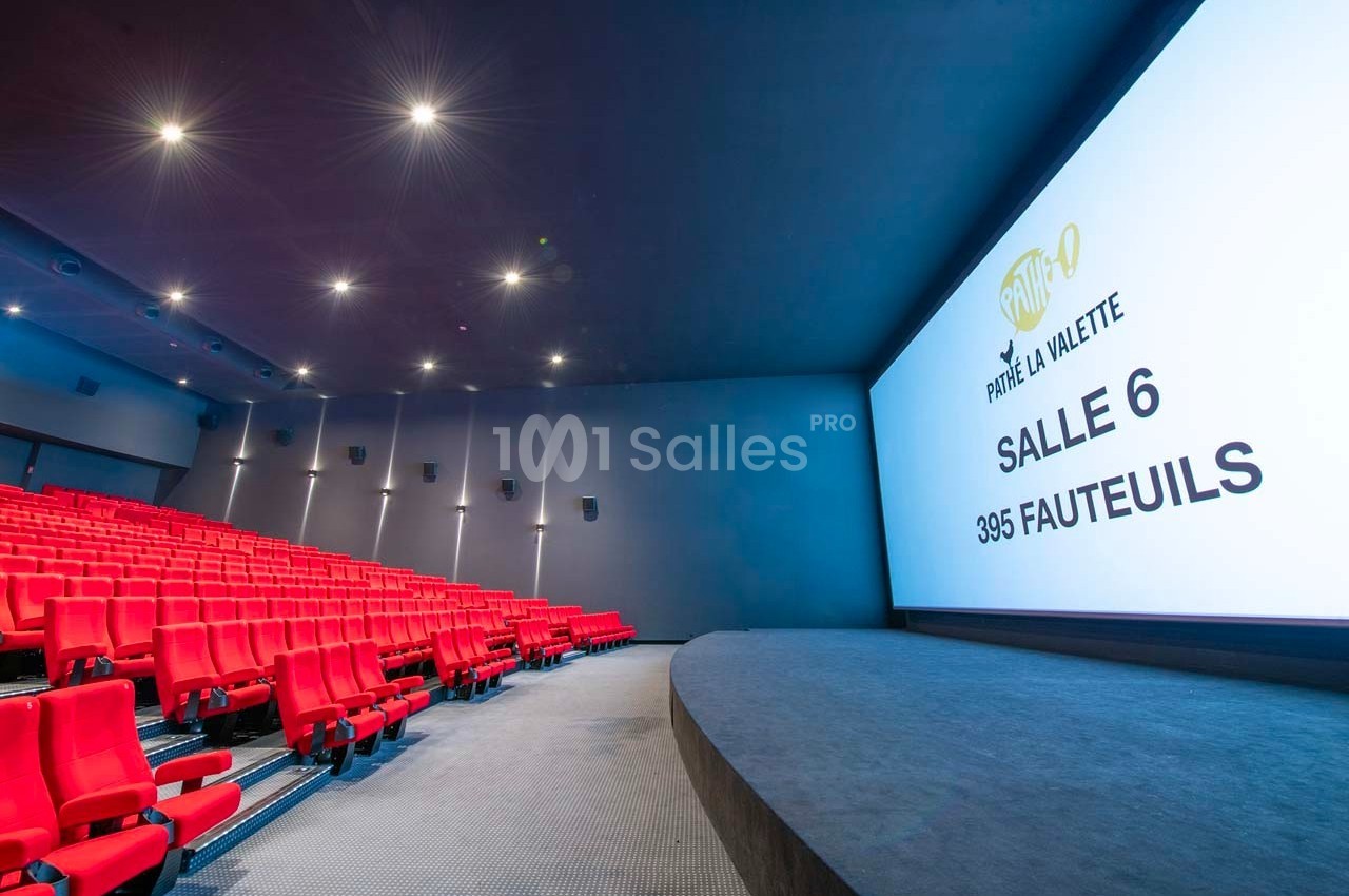 Salle de cinéma moderne avec des rangées de fauteuils rouges et un écran affichant des informations sur la salle.