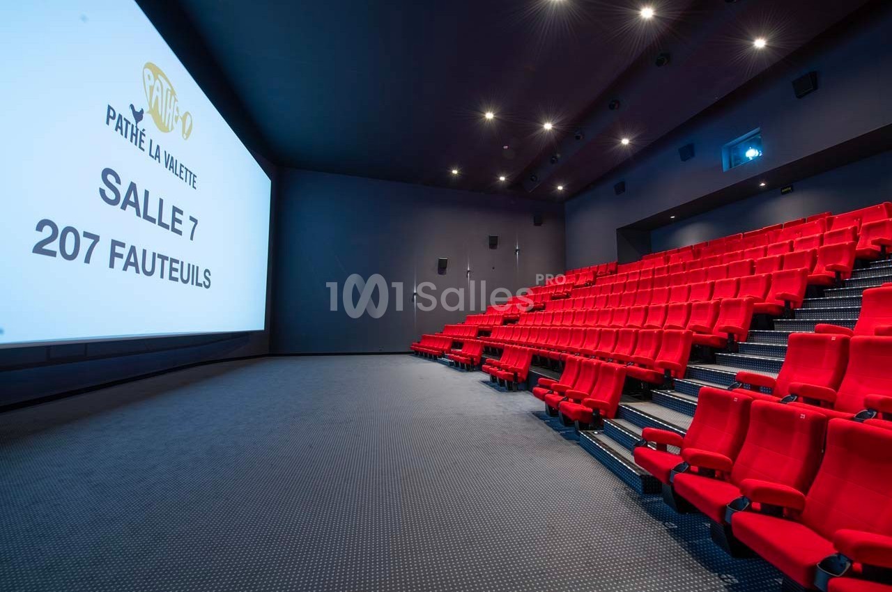 Salle de cinéma moderne avec des rangées de sièges rouges et un grand écran affichant ’Salle 7, 207 fauteuils’.