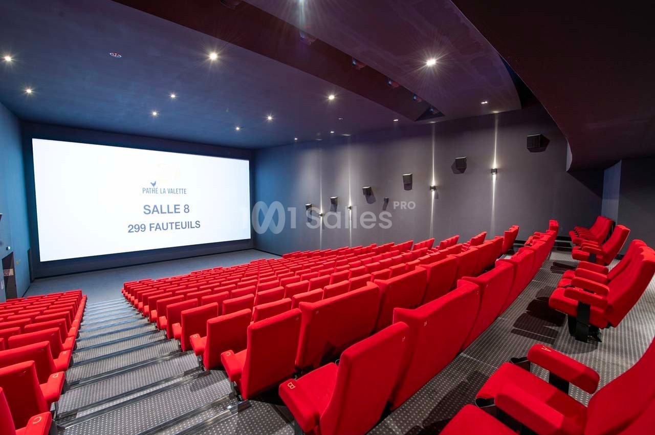 Salle de cinéma moderne avec sièges rouges alignés face à un grand écran blanc affichant des informations.