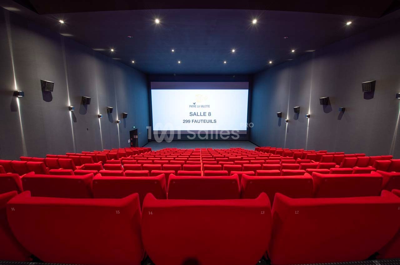 Salle de cinéma vide avec des rangées de fauteuils rouges et un écran affichant ’Salle 8, 299 fauteuils’.