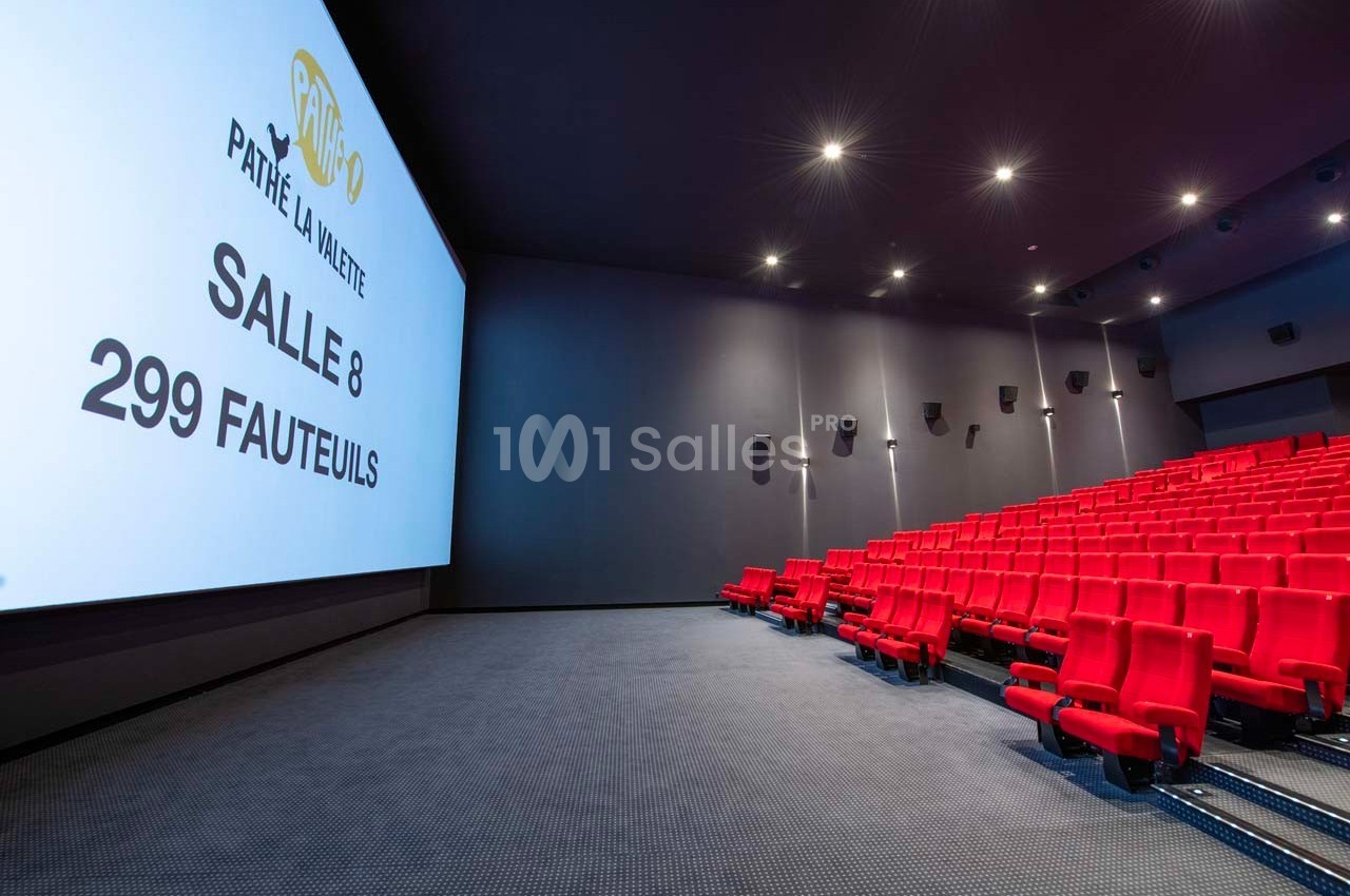 Salle de cinéma moderne avec écran géant, rangées de fauteuils rouges et éclairage tamisé.