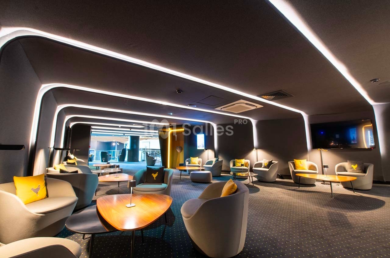 Espace lounge moderne avec fauteuils, tables basses en bois, éclairage LED et ambiance feutrée.