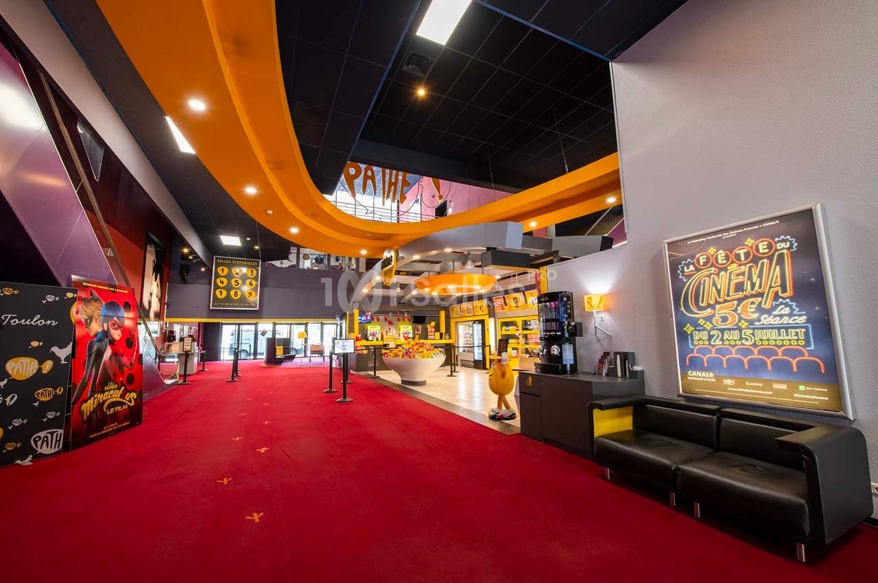 Hall d'entrée d'un cinéma avec tapis rouge, affiches promotionnelles et comptoir de confiseries lumineux.