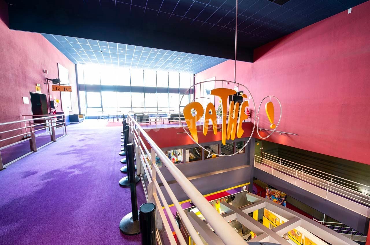 Hall d'entrée d'un cinéma Pathé avec moquette violette, balustrades métalliques et grande baie vitrée.
