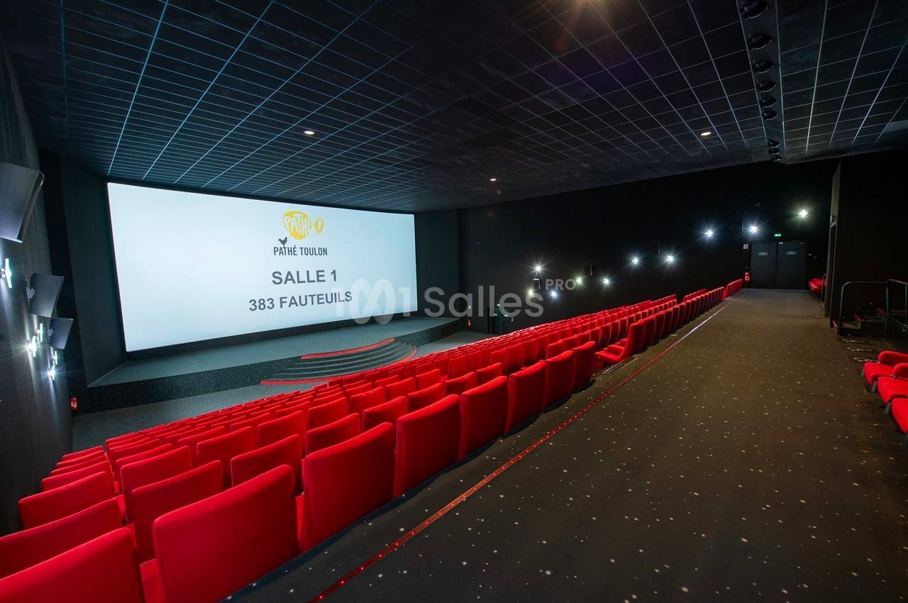 Salle de cinéma moderne avec des rangées de fauteuils rouges, un écran géant et un sol en moquette sombre.