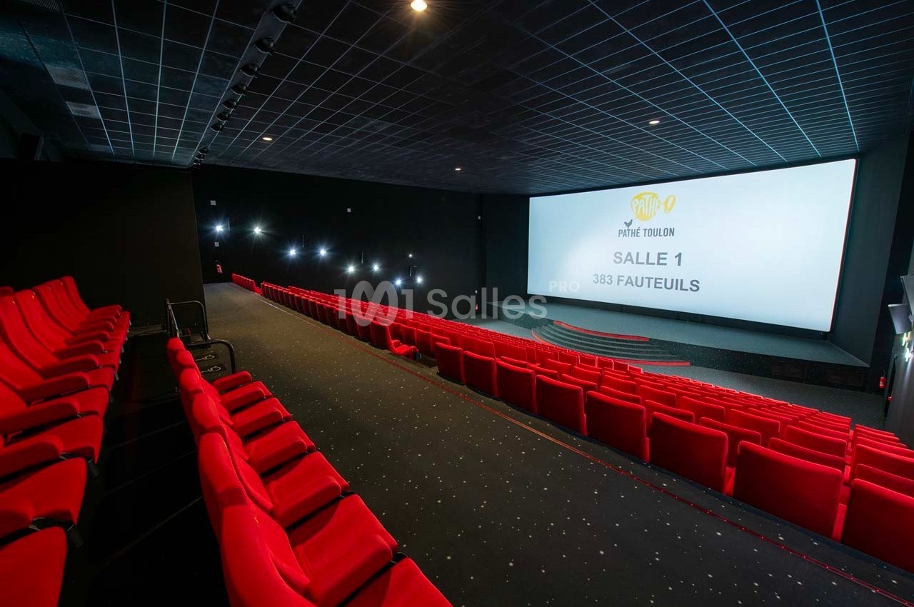 Salle de cinéma vide avec des rangées de fauteuils rouges et un grand écran affichant des informations sur la salle.