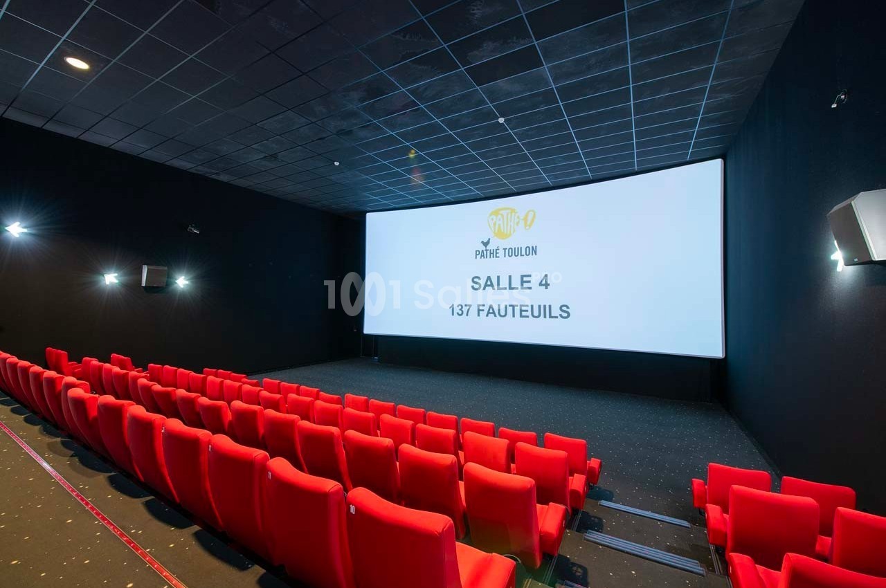 Salle de cinéma vide avec écran affichant ’Salle 4, 137 fauteuils’, rangées de sièges rouges et éclairage tamisé.