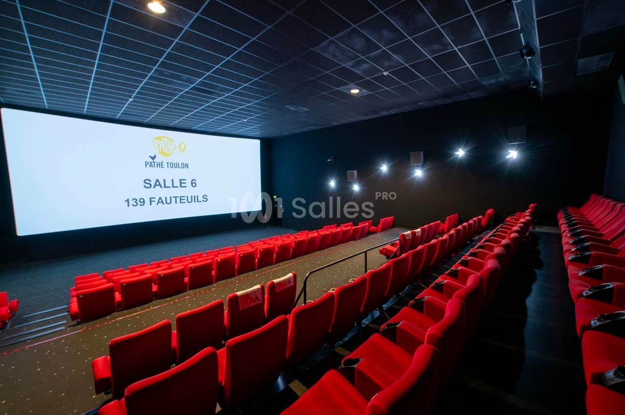 Salle de cinéma avec des rangées de fauteuils rouges, un grand écran blanc affichant des informations sur la salle.