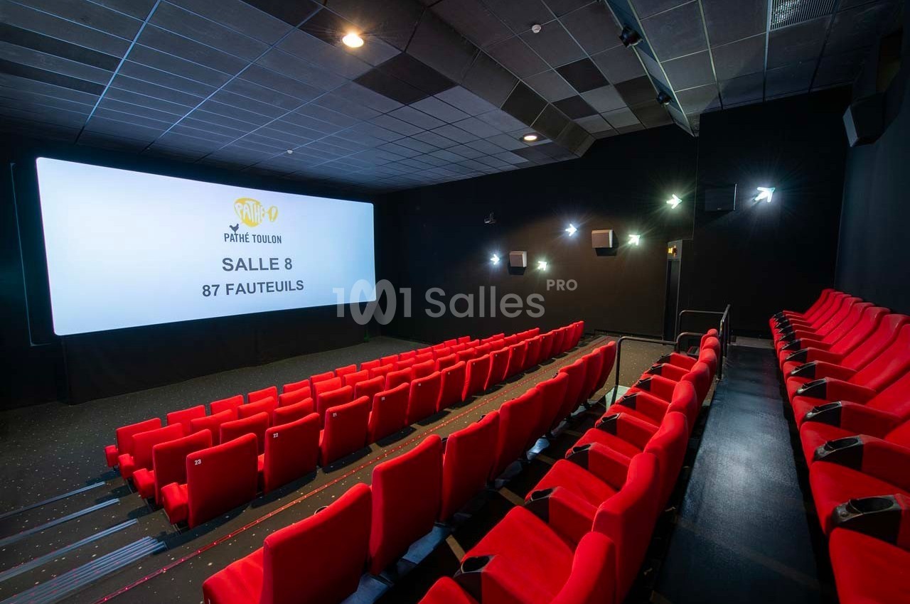 Salle de cinéma avec écran large, rangées de fauteuils rouges et éclairage tamisé.