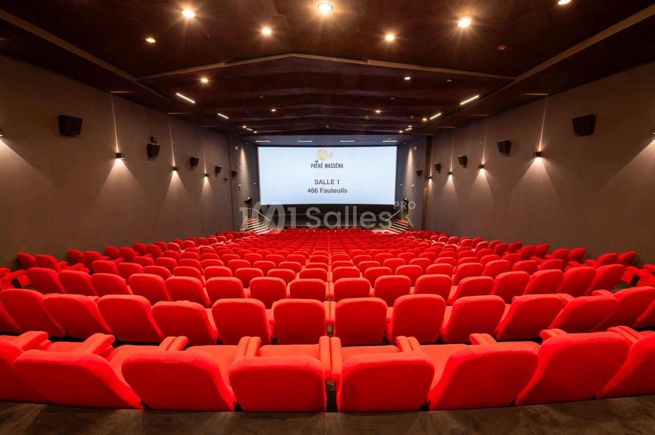 Salle de cinéma vide avec des rangées de fauteuils rouges et un écran blanc au fond.