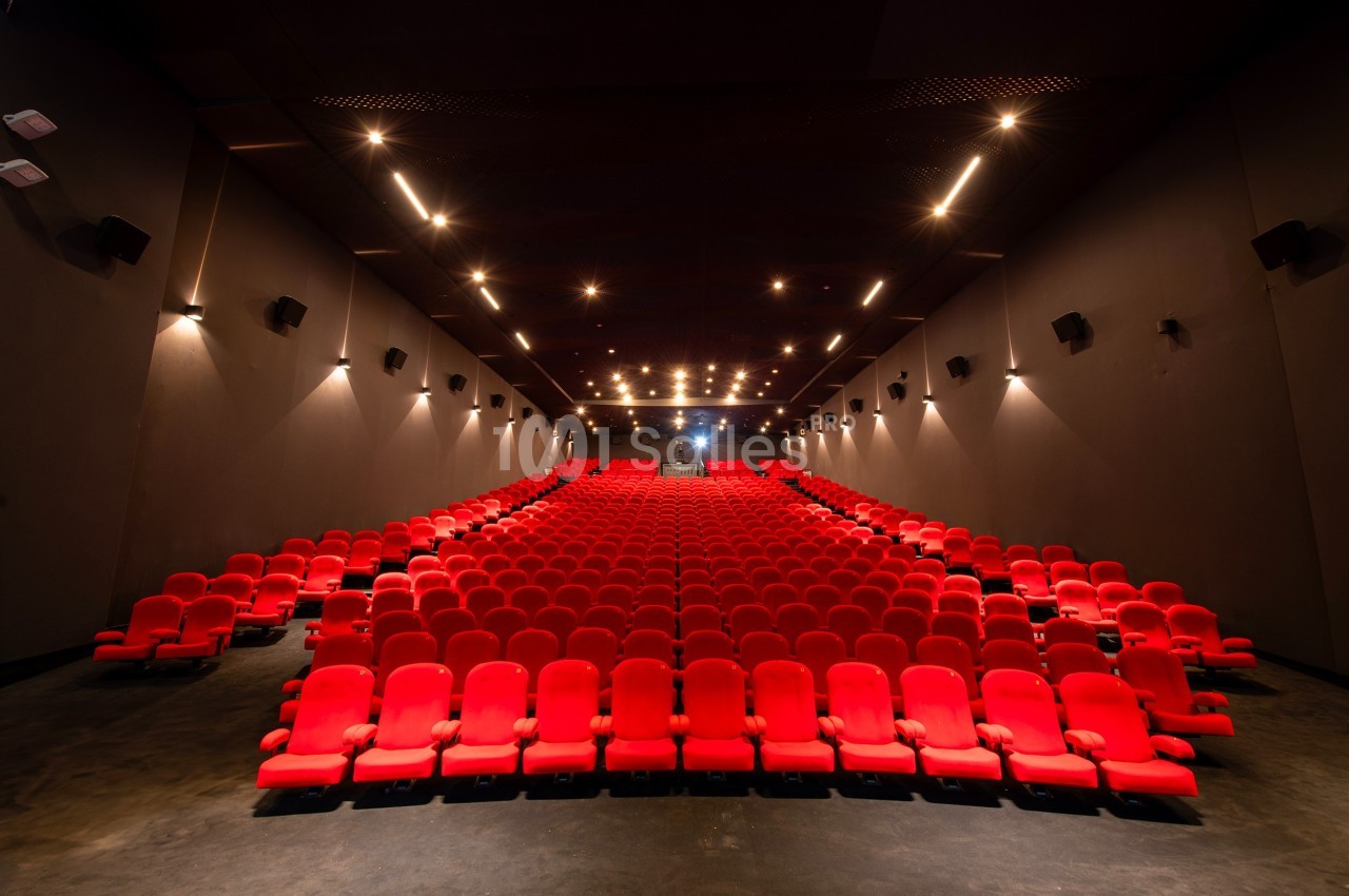 Salle de cinéma vide avec des rangées de fauteuils rouges et un éclairage tamisé.