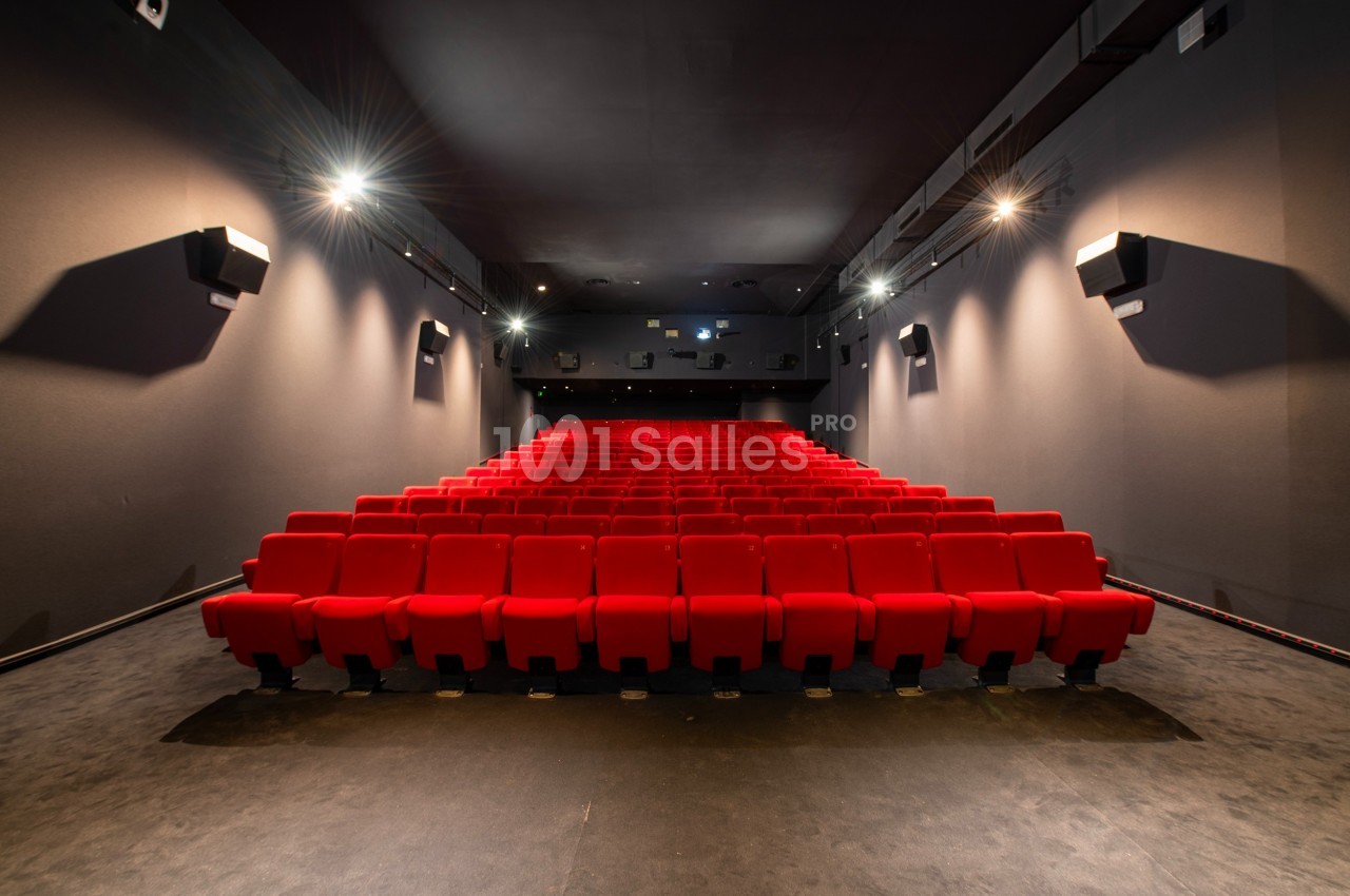 Salle de cinéma vide avec rangées de fauteuils rouges alignés et éclairage tamisé.