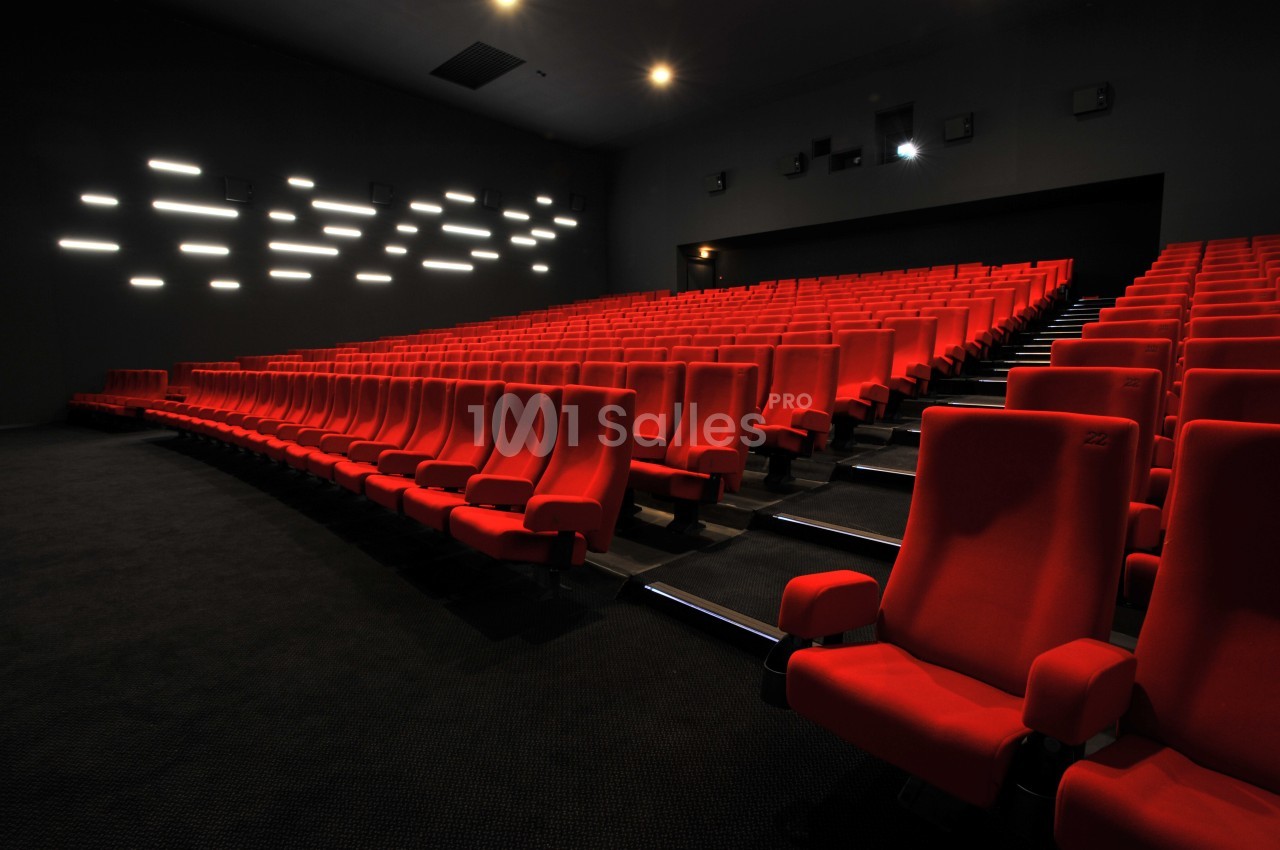 Salle de cinéma vide avec des rangées de fauteuils rouges et un éclairage mural discret.