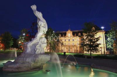 Façade moderne d'un bâtiment avec des murs en verre et acier rouillé, sous un ciel partiellement nuageux.
