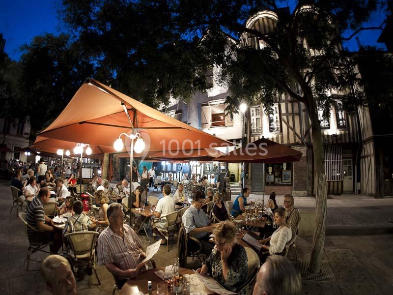 Terrasse d'un restaurant animé en soirée, avec des clients attablés sous des parasols et des lampes suspendues.