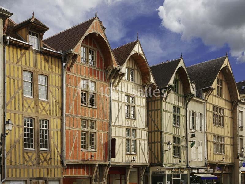 Maisons à colombages colorées alignées dans une rue sous un ciel partiellement nuageux.
