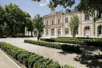 Façade moderne d'un bâtiment avec des murs en verre et acier rouillé, sous un ciel partiellement nuageux.