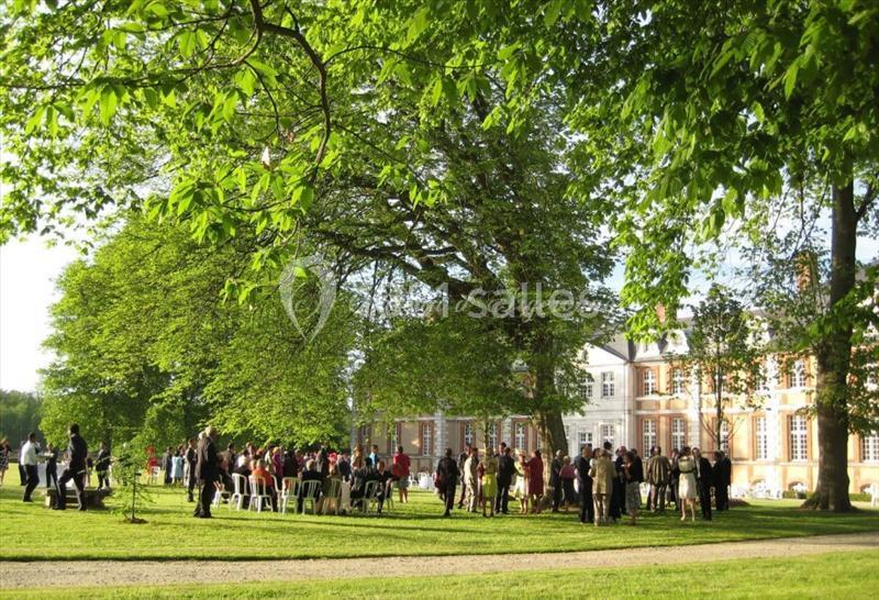 Groupe de personnes rassemblées dans un parc verdoyant devant un bâtiment historique par une journée ensoleillée.