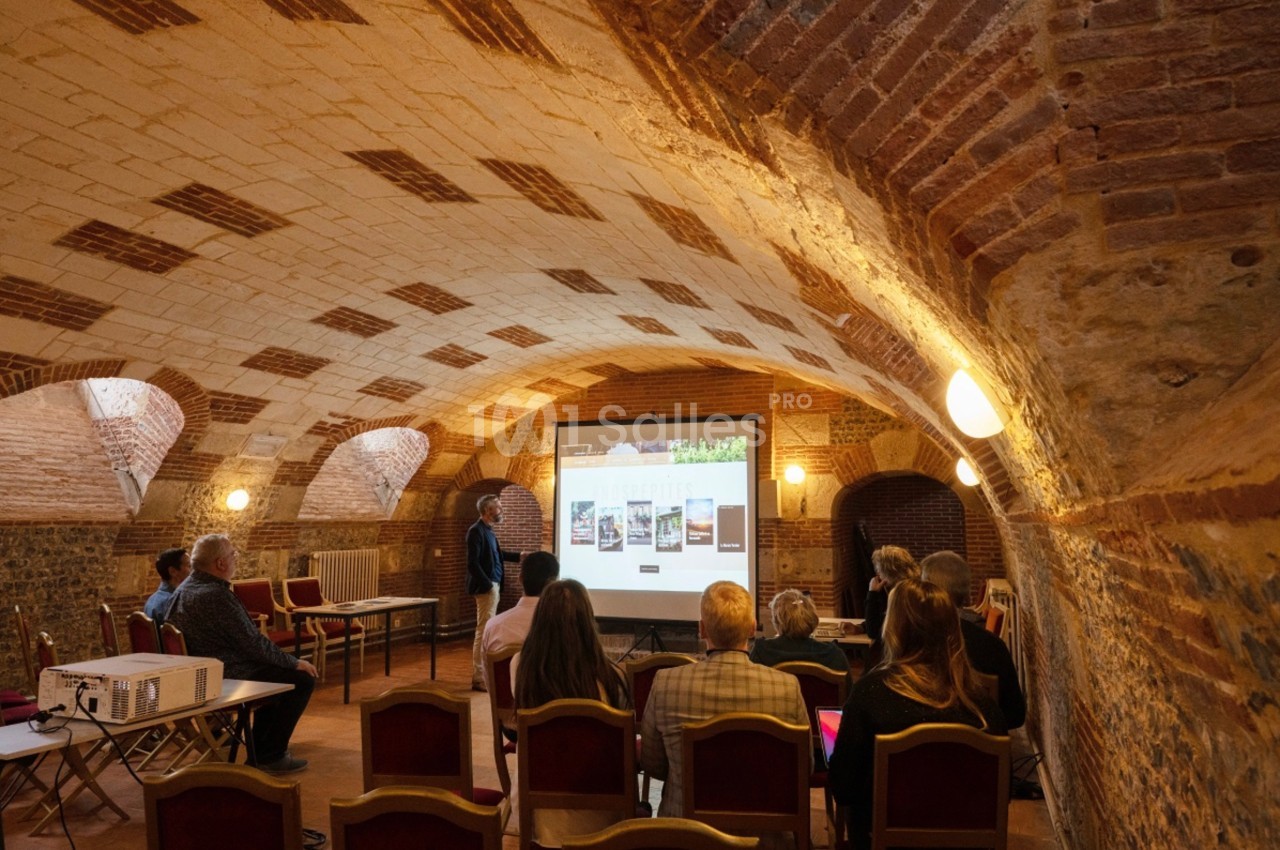 Un groupe de personnes assises dans une salle voûtée en briques, regardant une présentation projetée sur un écran.