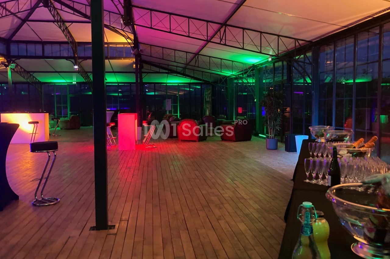 Salle avec parquet, mobilier lounge et éclairage coloré, préparée pour un événement avec buffet et boissons.