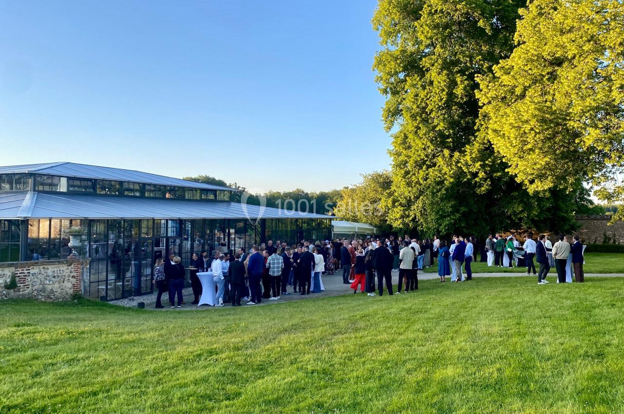Groupe de personnes rassemblées près d'une verrière moderne dans un jardin verdoyant par temps ensoleillé.