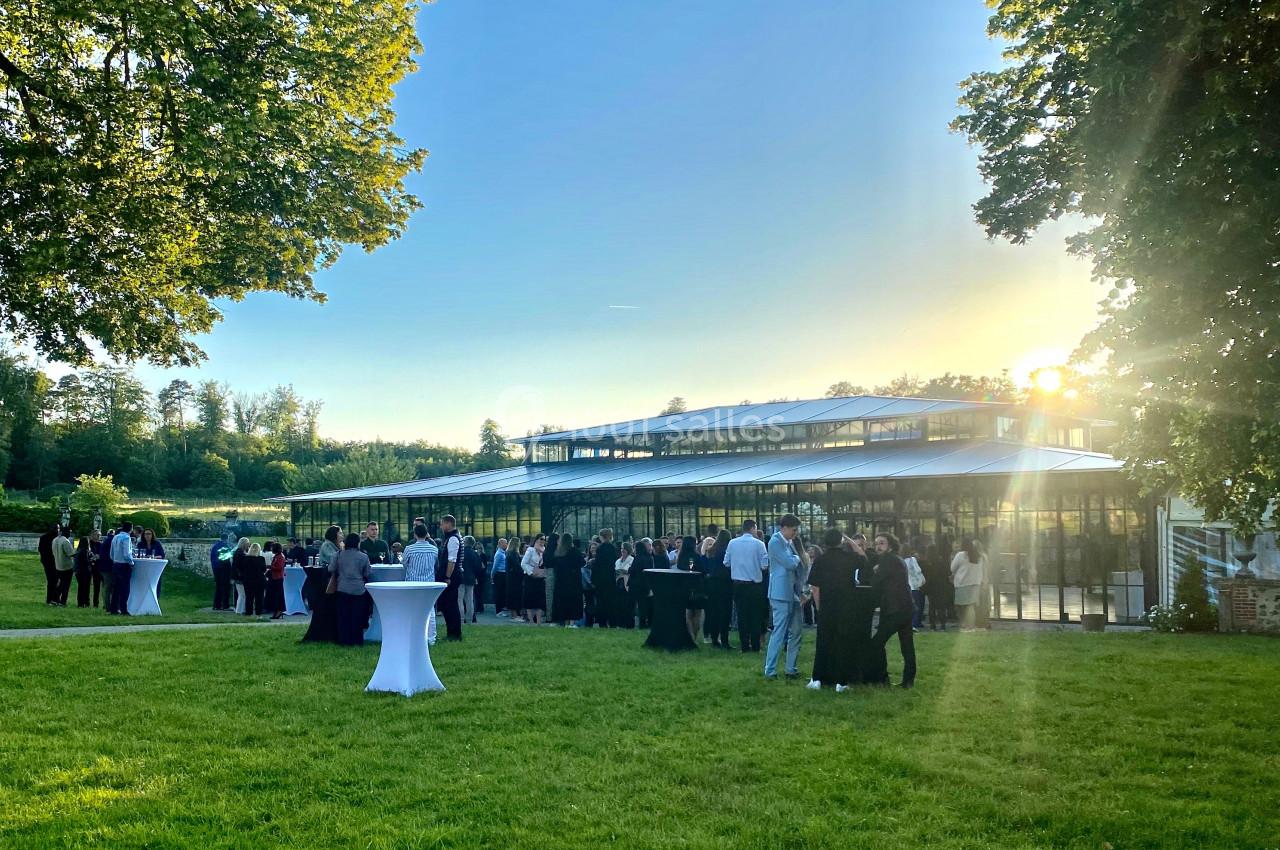 Groupe de personnes rassemblées sur une pelouse devant un bâtiment vitré au coucher du soleil.