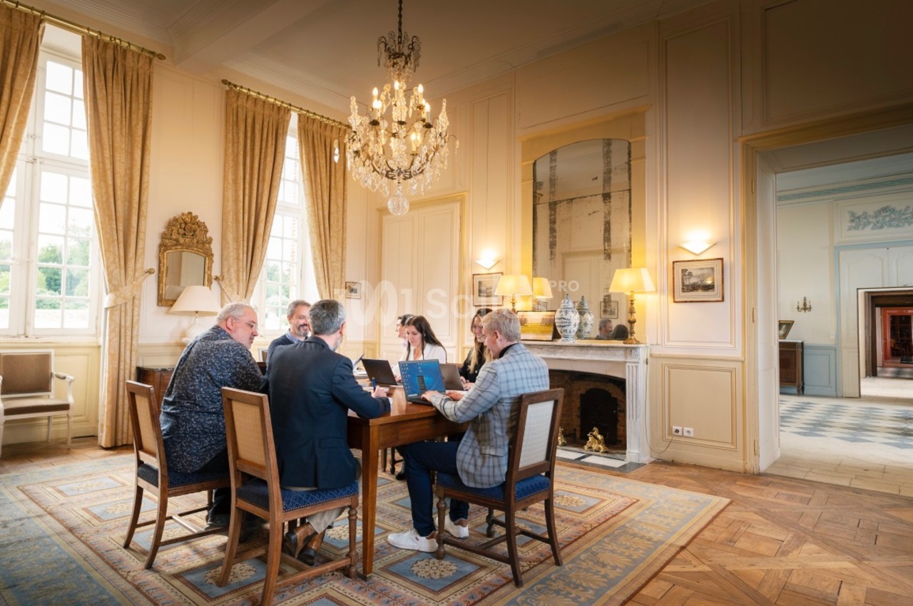 Un groupe de personnes assises autour d'une table dans une salle élégante avec lustre et grandes fenêtres.