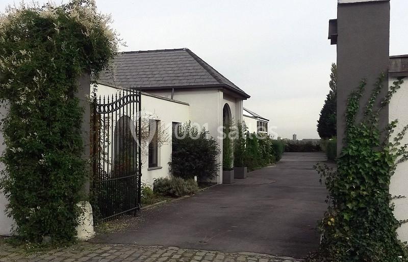 Entrée d'une propriété avec portail en fer forgé, murs blancs, toiture en ardoise et végétation grimpante.