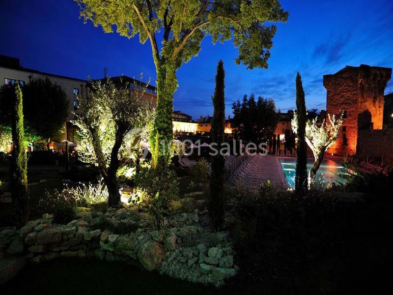 Location salle Aix-en-Provence (Bouches-du-Rhône) - Hôtel Aquabella & Spa #12 Jardin éclairé de nuit avec piscine, arbres illuminés et bâtiments en arrière-plan sous un ciel bleu foncé.