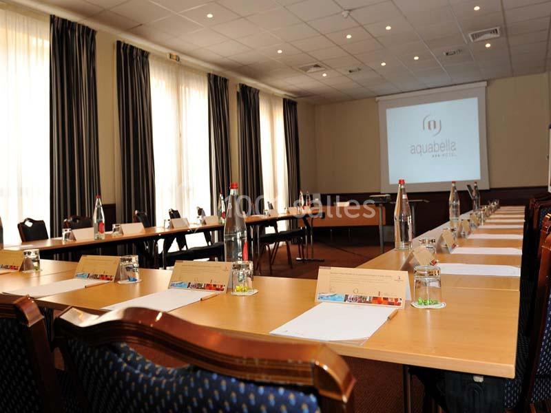 Location salle Aix-en-Provence (Bouches-du-Rhône) - Hôtel Aquabella & Spa #4 Salle de réunion lumineuse avec une grande table en U, des chaises, des bouteilles d'eau et un écran de projection.