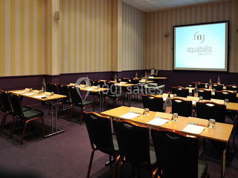 Location salle Aix-en-Provence (Bouches-du-Rhône) - Hôtel Aquabella & Spa #3 Salle de réunion équipée de tables, chaises, bouteilles d'eau, bloc-notes et écran de projection allumé.