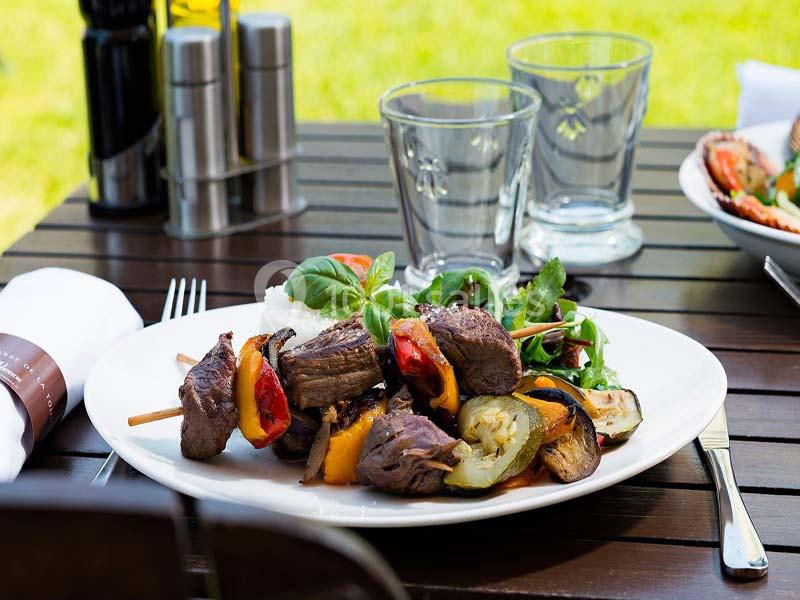 Location salle Aix-en-Provence (Bouches-du-Rhône) - Hôtel Aquabella & Spa #15 Assiette de brochettes de viande grillée avec légumes, accompagnée de salade verte, servie sur une table en extérieur.