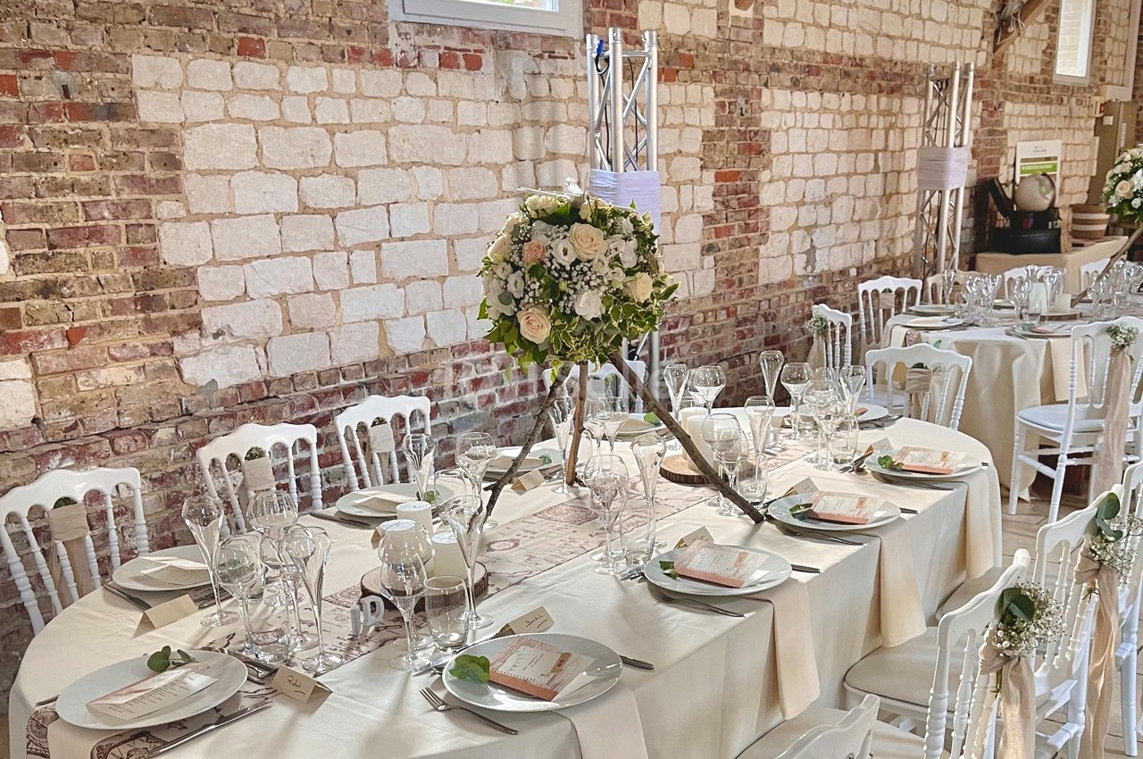 Salle de réception décorée avec des tables dressées, nappes blanches, vaisselle élégante et centre de table floral.