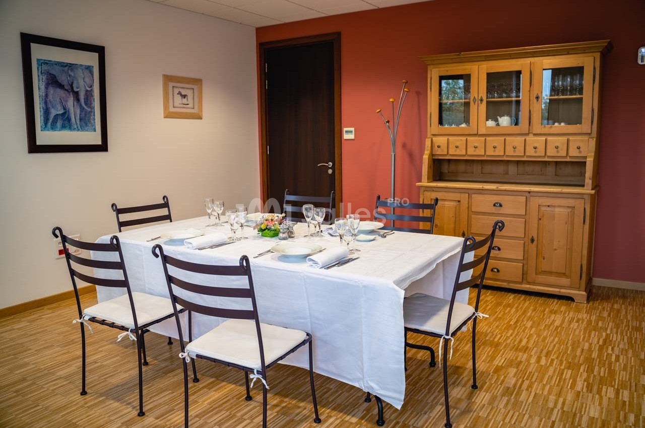 Salle à manger avec table dressée pour six personnes, buffet en bois et murs décorés de tableaux.