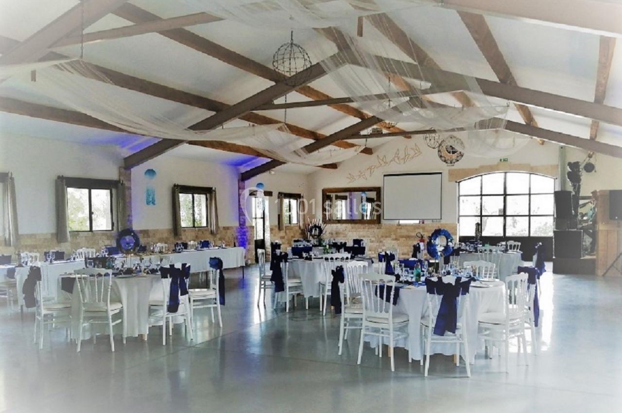 Salle de réception décorée avec des tables rondes dressées, nappes blanches et chaises ornées de rubans bleus.