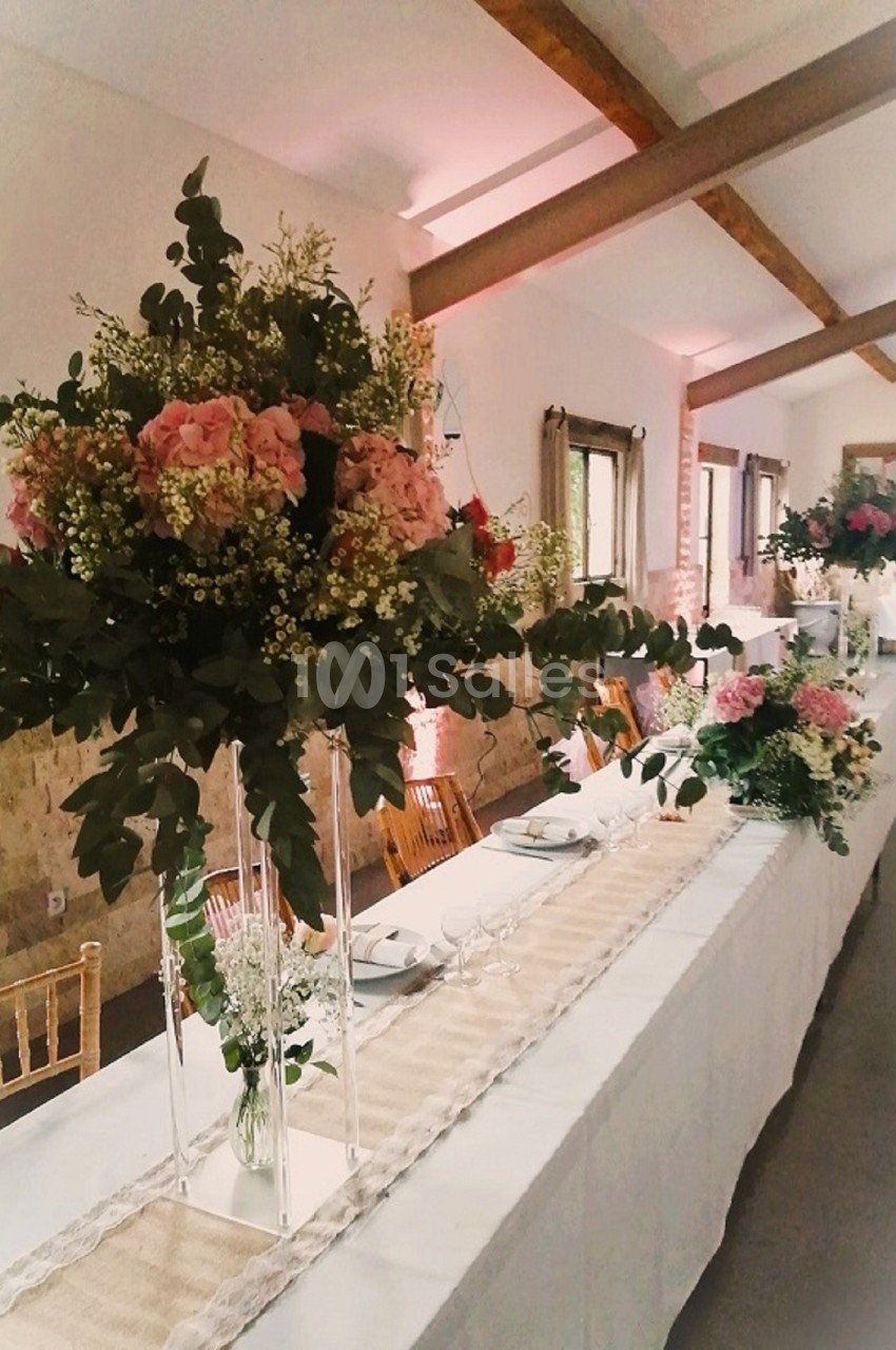 Grande table de réception décorée de chemins de table en lin et de bouquets de fleurs roses et vertes sur supports hauts.