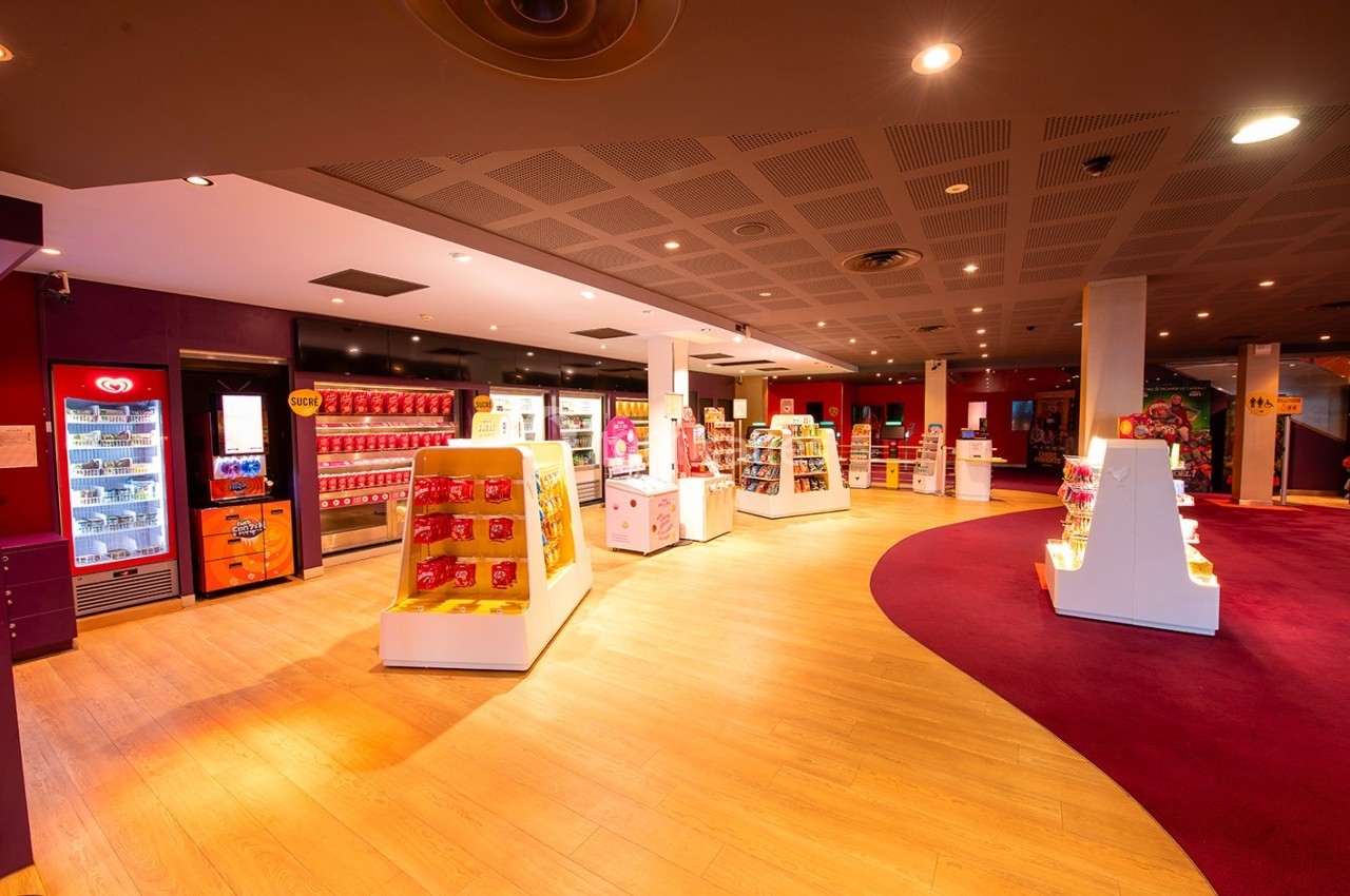 Vue d'une boutique lumineuse avec des étagères remplies de produits colorés et un sol en bois clair.