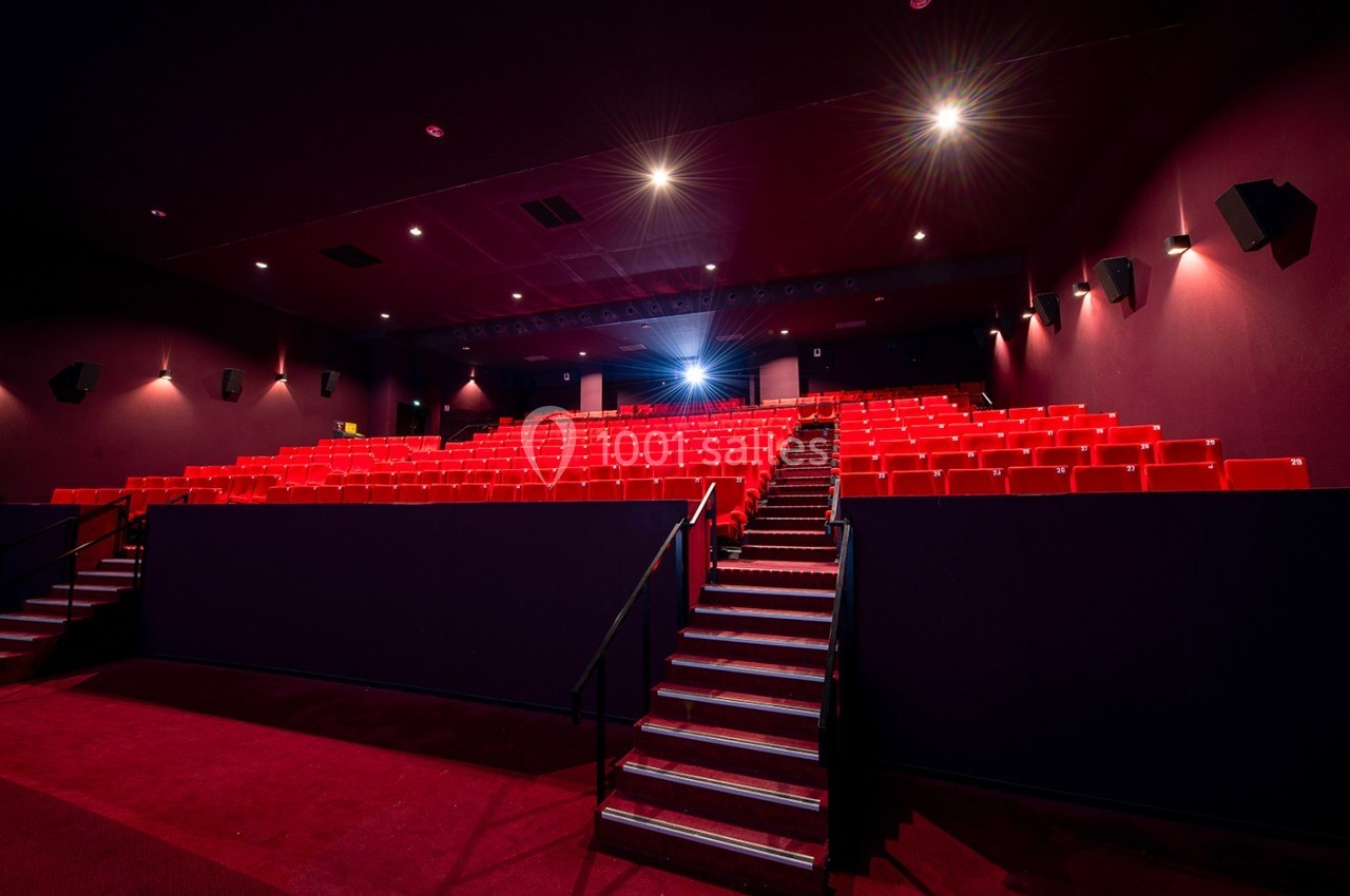 Salle de cinéma vide avec des rangées de sièges rouges, éclairée par des lumières tamisées.
