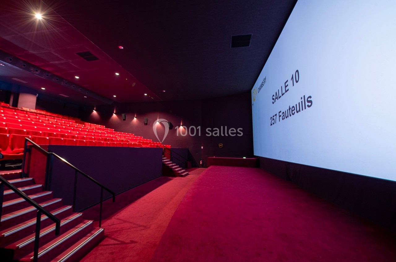 Salle de cinéma vide avec sièges rouges, écran géant affichant ’Salle 10, 257 fauteuils’ et allée centrale.