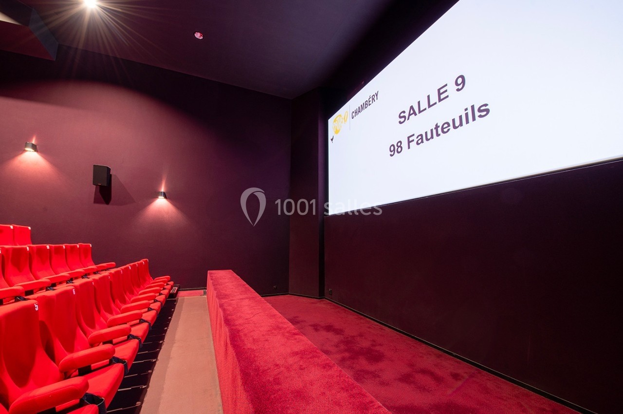Salle de cinéma avec des fauteuils rouges alignés et un écran affichant ’Salle 9, 96 fauteuils’ dans un décor sombre.