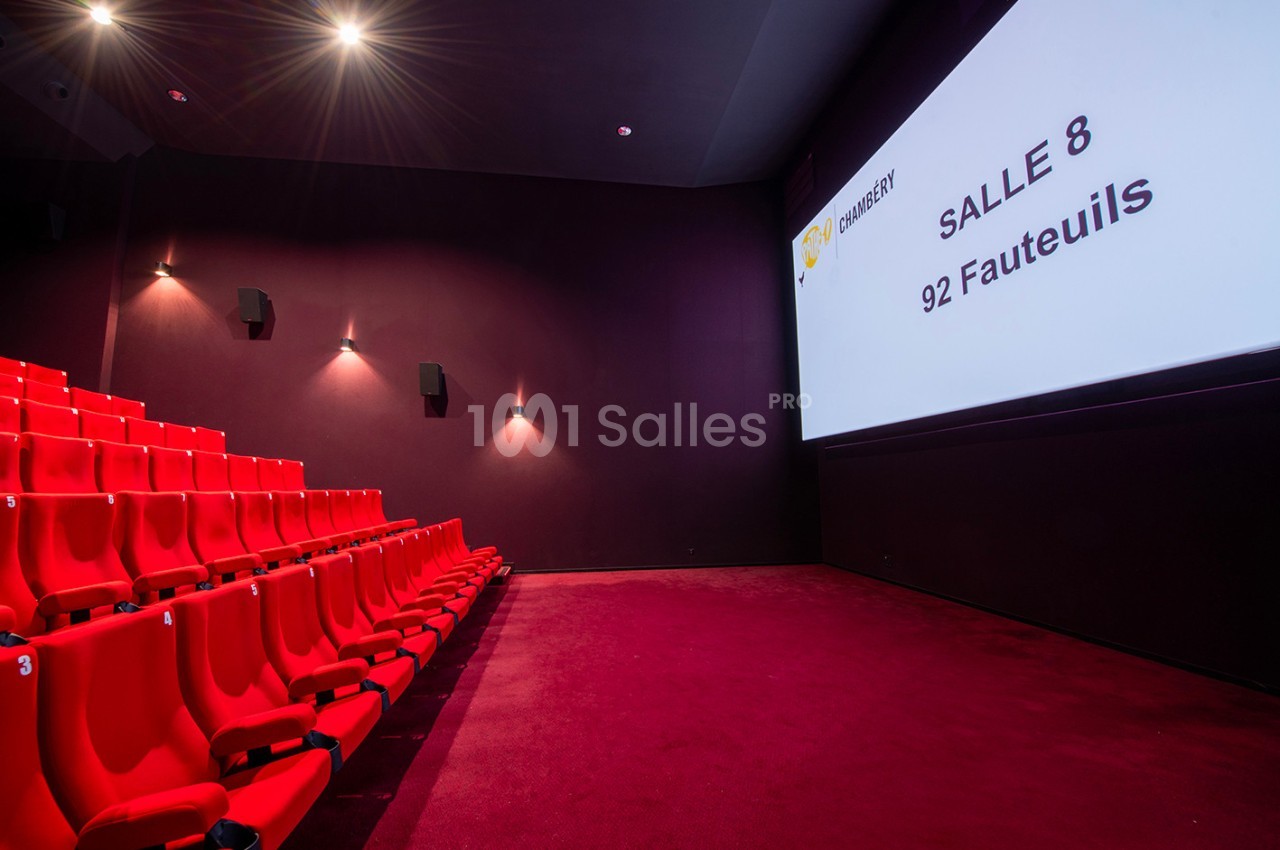 Salle de cinéma moderne avec sièges rouges alignés et écran affichant ’Salle 8, 92 fauteuils’.
