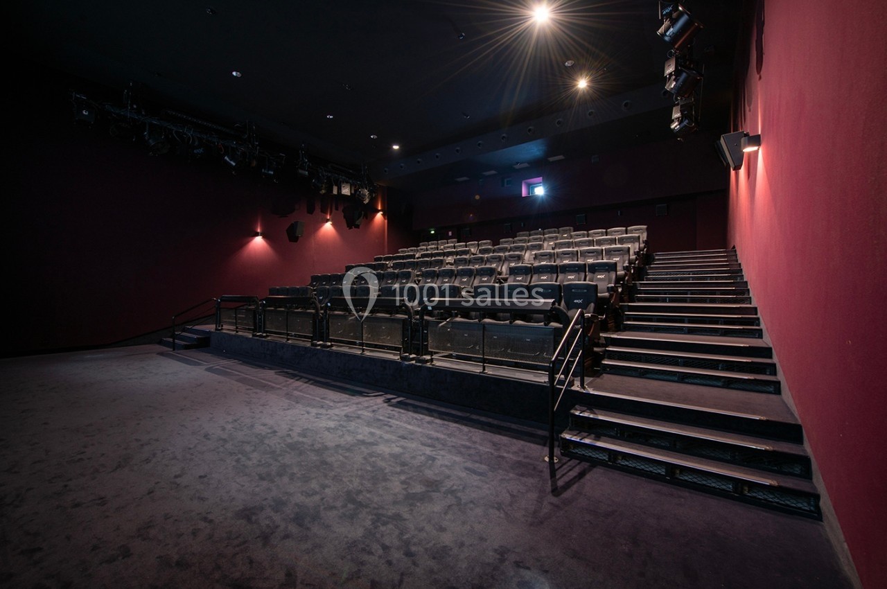 Salle de cinéma vide avec rangées de sièges en gradins, éclairage tamisé et murs rouges.