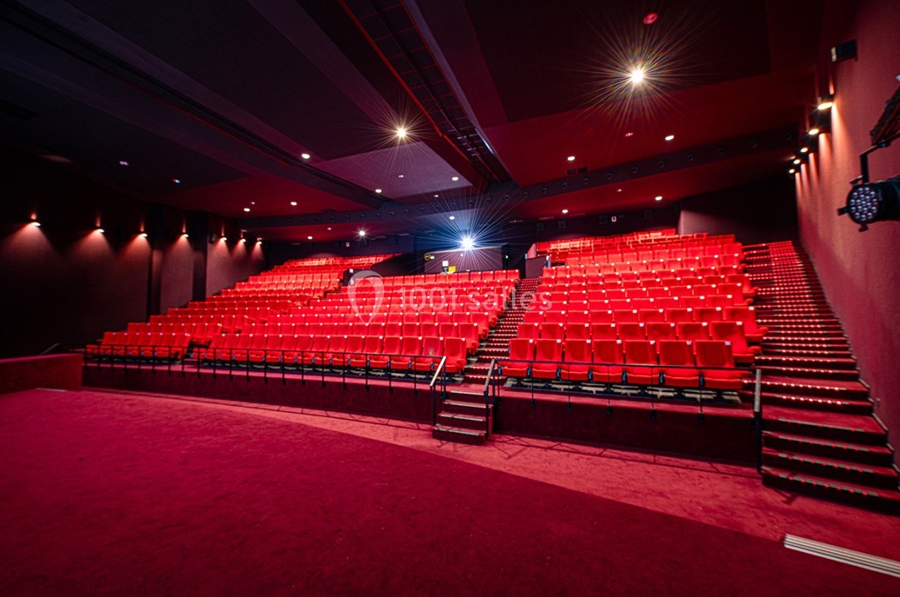 Salle de cinéma vide avec des rangées de sièges rouges, éclairage tamisé et écran non visible.