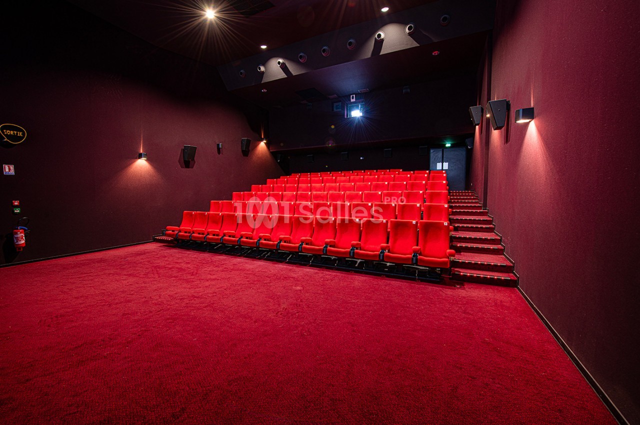 Salle de cinéma vide avec rangées de sièges rouges, éclairage tamisé et moquette rouge au sol.