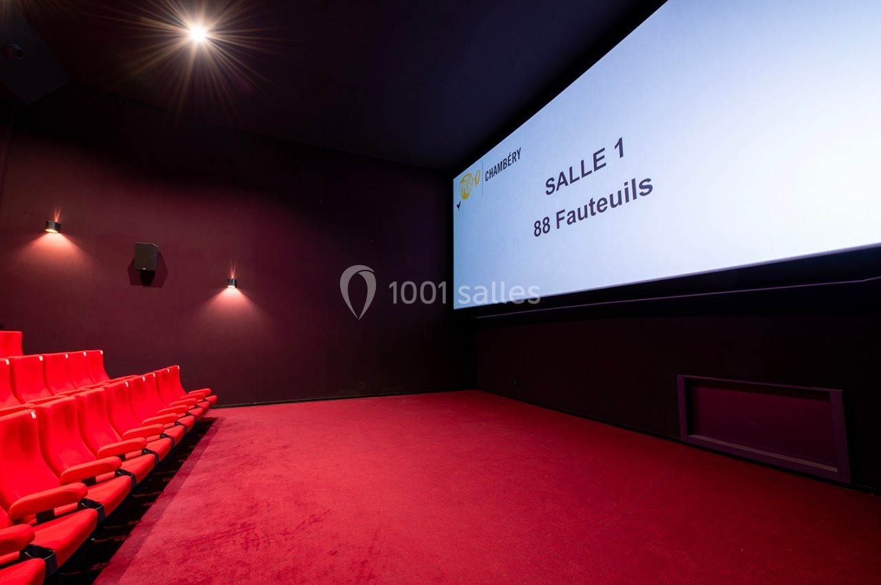 Salle de cinéma vide avec des sièges rouges, un écran affichant ’Salle 1, 88 fauteuils’ et un éclairage tamisé.