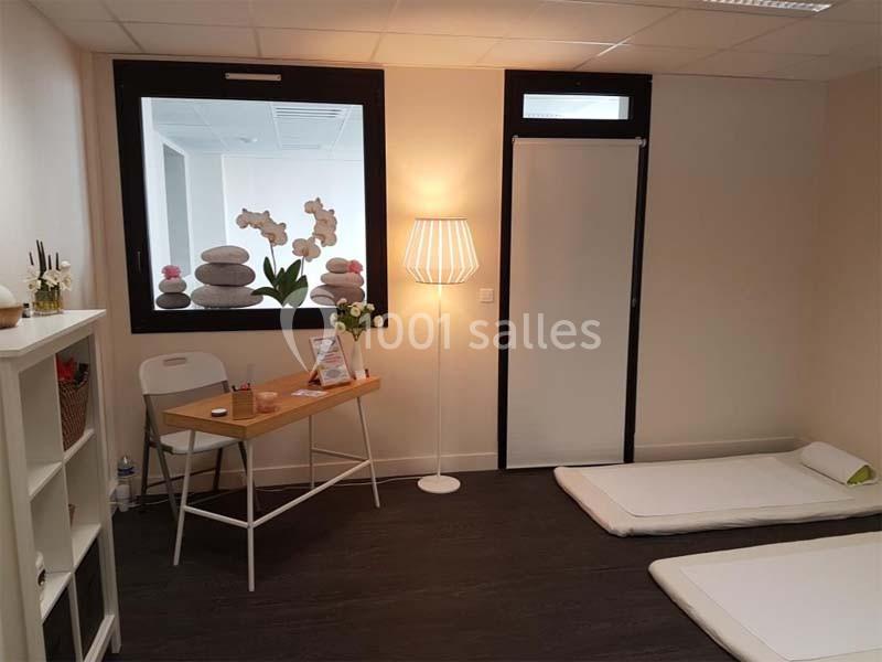 Salle de bien-être avec matelas au sol, bureau en bois, lampe, étagère et décoration zen.
