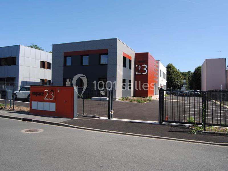 Bâtiment moderne à deux étages avec façade grise et rouge, entouré d'un parking et clôturé par une grille noire.