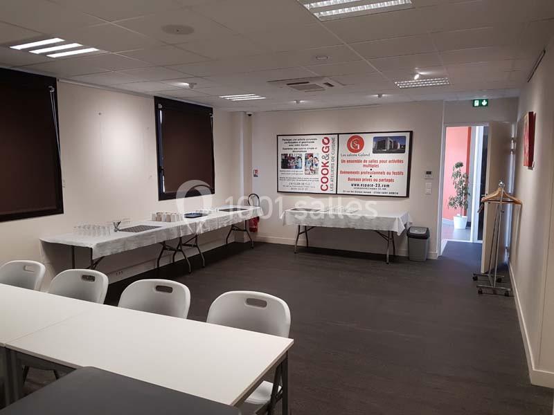 Salle de réunion équipée de tables, chaises et buffets, avec éclairage artificiel et fenêtres partiellement occultées.