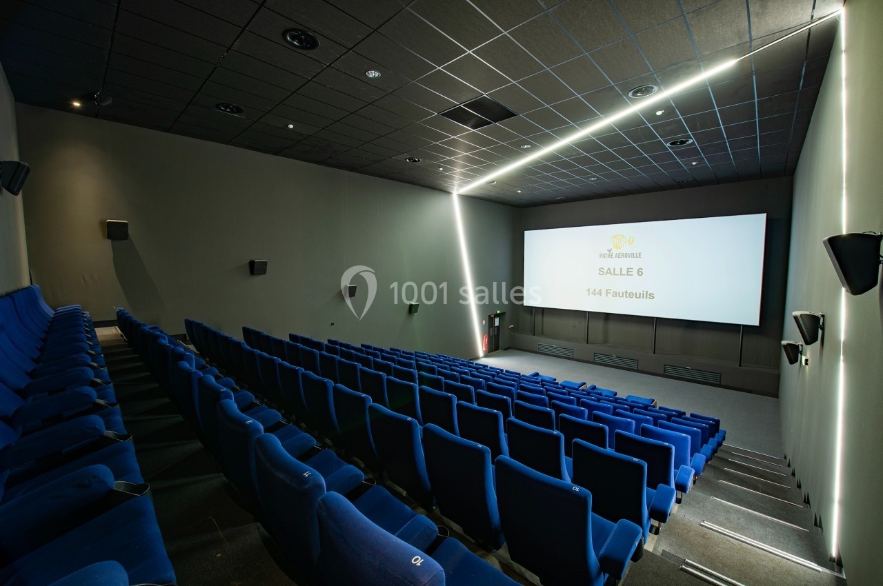 Salle de cinéma vide avec des rangées de fauteuils bleus et un écran blanc affichant ’Salle 6, 144 fauteuils’.