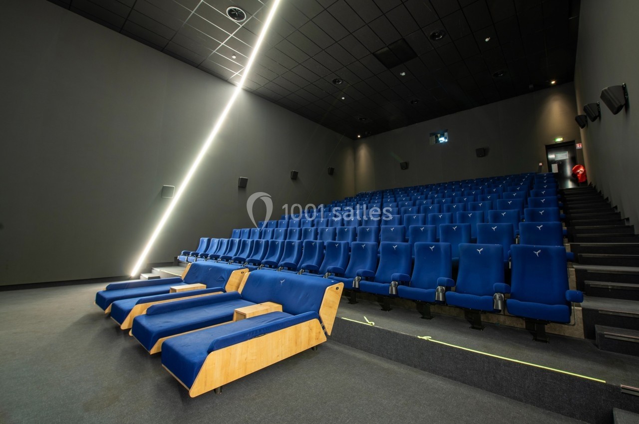Salle de cinéma moderne avec rangées de sièges bleus et quelques fauteuils inclinables au premier plan.